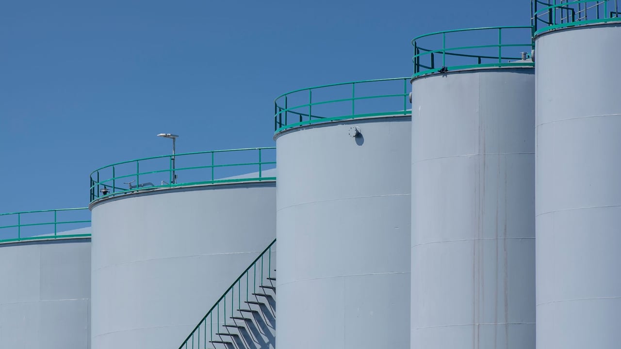 Large industrial storage tanks with green railings against a clear blue sky.
