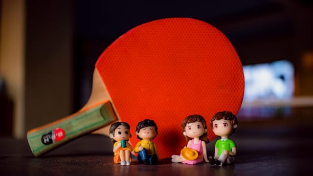 Small colorful figurines of couples placed on table near professional red table tennis racket in light room on blurred background