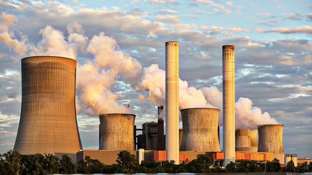 View of a power plant with smoke emissions under a cloudy sky, depicting industrial energy production.