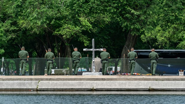 Military personnel participate in a solemn ceremony near a cross monument in Washington D.C. park.