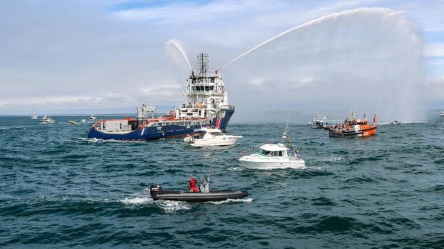 A vibrant display of boats in a parade on the sea near Granville, Normandie, with water sprays creating an energetic scene.