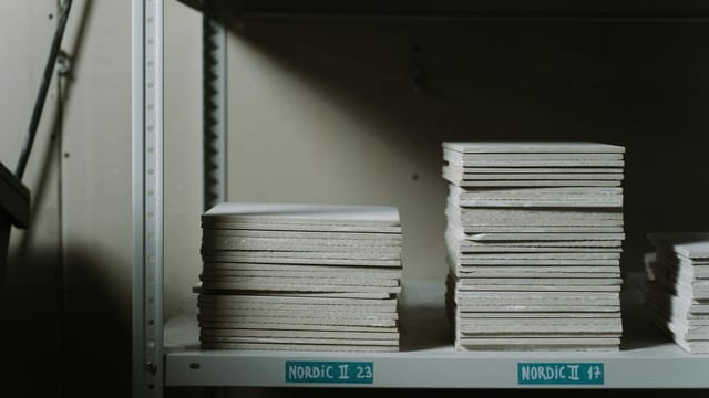 Stacks of ceramic tiles neatly arranged on industrial shelves in a dimly lit warehouse.