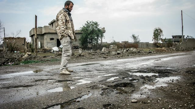 A solitary man walks on a war-ravaged street in Salah ad Din, Iraq amidst destruction.