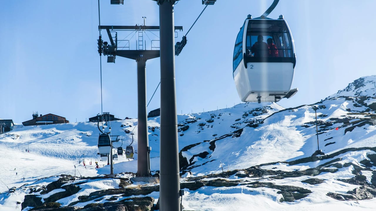 Cable cars transport skiers over a snowy alpine landscape on a bright winter day.