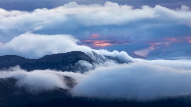 A serene view of misty mountain peaks cloaked in clouds at twilight, offering a tranquil nature scene.