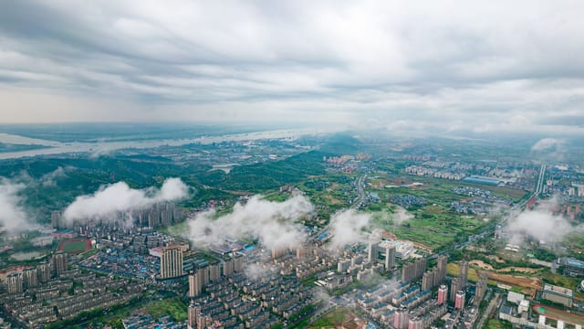 Stunning aerial view of a city in China with green landscapes and cloud coverage, showcasing urban and rural blend.