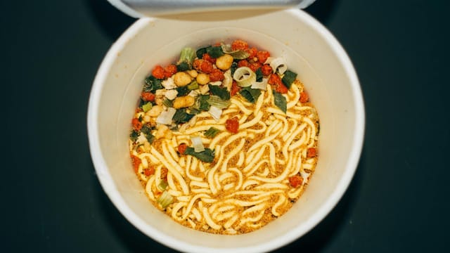 Top-down view of instant noodle cup with vibrant dehydrated ingredients ready for cooking.