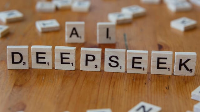 Wooden Scrabble tiles spelling 'DEEPSEEK' with 'AI' on a wooden table, illustrating AI concepts creatively.