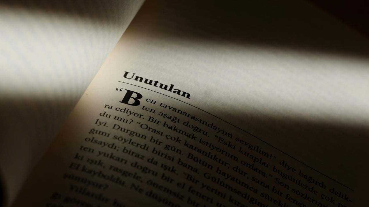 Moody close-up photo of a book page partially lit, highlighting text in Turkish.