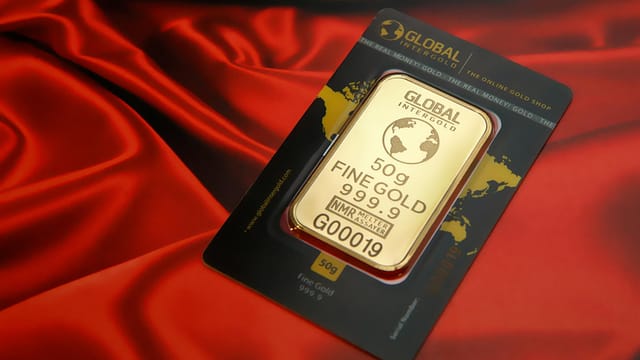 A 50g fine gold bar displayed elegantly on a rich red fabric background, symbolizing wealth and luxury.