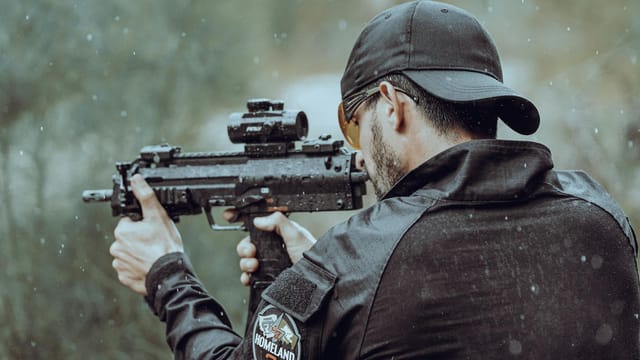 Man aiming with tactical gear and firearm in an outdoor setting during rain.