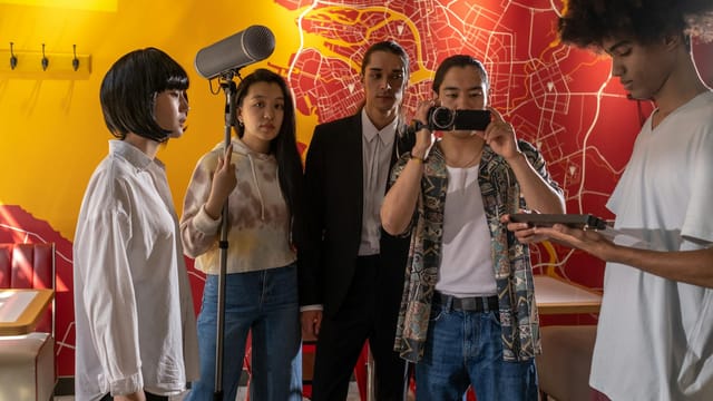 Film crew in action capturing an indoor movie scene with microphones and cameras, diverse cast.