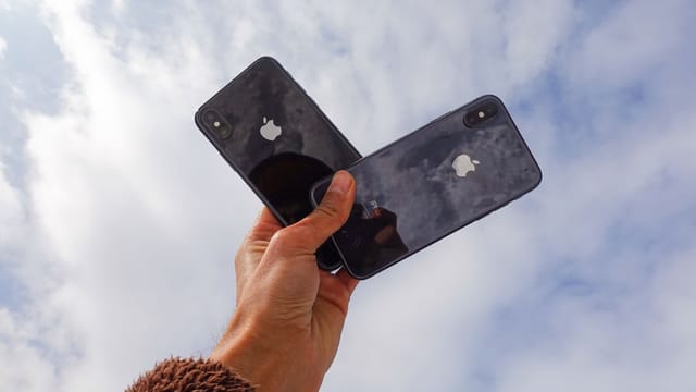 Close-up of a hand holding two smartphones against a cloudy sky, showcasing modern technology.