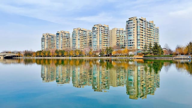 High-rise apartments reflect on a tranquil waterfront in Zhengzhou, China, showcasing urban architecture.