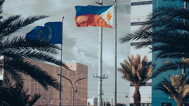 Philippine and other flags waving amidst cityscape buildings and palm trees.