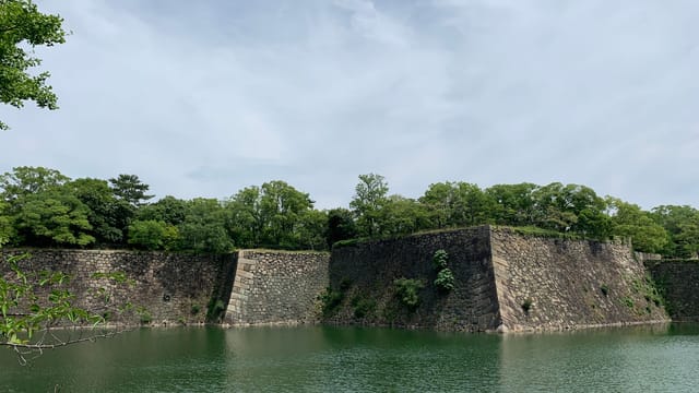 Scenic view of a castle moat surrounded by lush greenery and historic stone walls in Osaka, Japan.