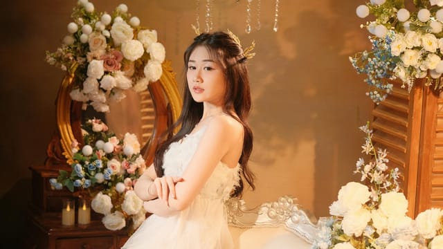 A woman posing elegantly surrounded by flowers indoors, exuding grace.