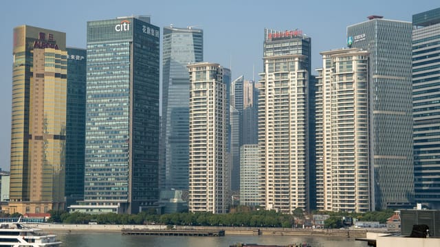 Sunlit view of Pudong's modern skyscrapers across the Huangpu River in Shanghai.