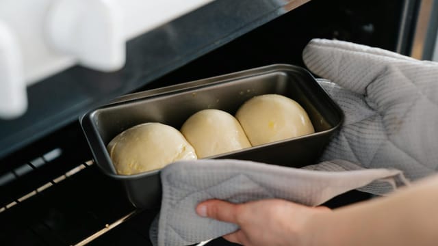 Close-up of a person placing homemade bread dough into an oven.