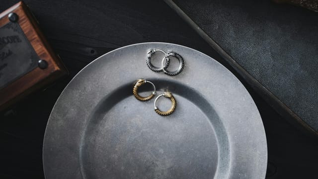 Stylish silver and gold hoop earrings arranged on a rustic metallic plate against a dark background.