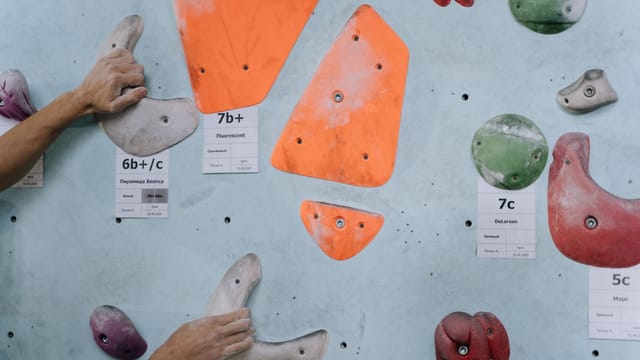 Hands gripping colorful climbing holds on an indoor climbing wall, highlighting strength and technique.