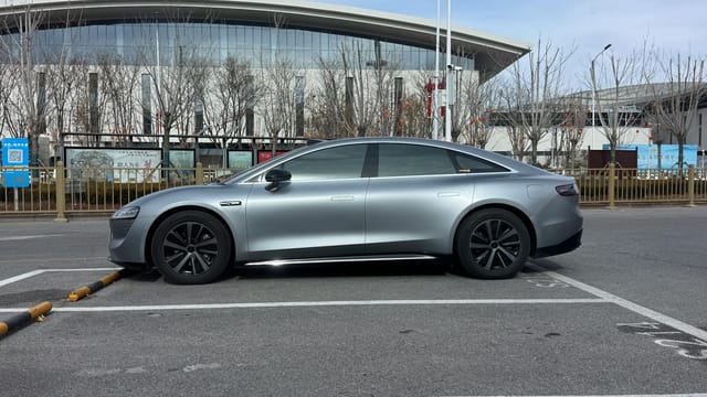 Side view of a sleek silver electric sedan parked in a city lot by a modern building.