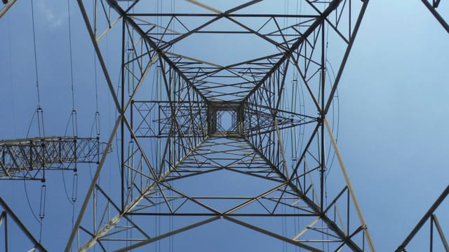 A striking low angle perspective of an electricity tower with a clear blue sky background.