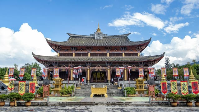 A beautifully adorned Chinese temple set against a blue sky, showcasing traditional architectural elements and cultural flags.
