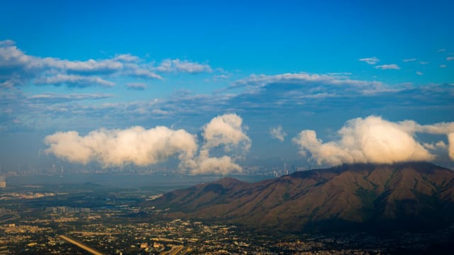 A breathtaking aerial view capturing the mountains and skyline of Hong Kong, under a vibrant blue sky.