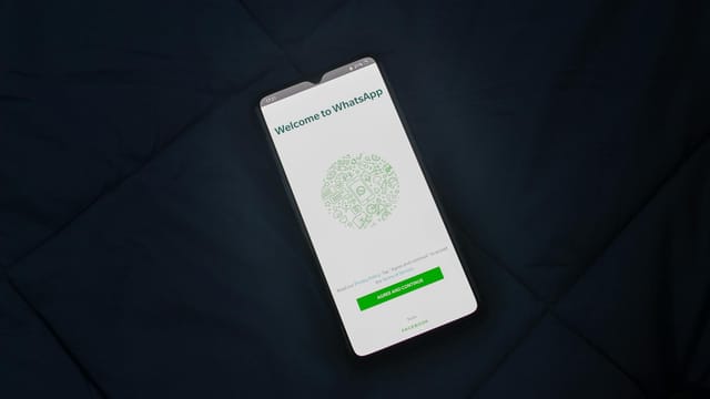 Smartphone displaying WhatsApp login screen on a dark surface. Overhead view.