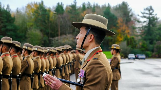 Gurkha soldiers in traditional uniforms stand in parade formation outdoors.