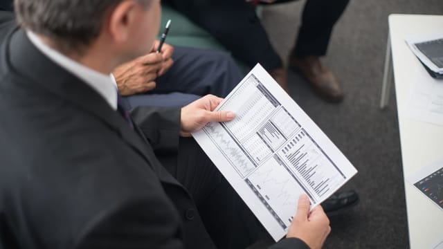 Two businessmen analyze financial documents during a meeting, focusing on data trends and performance.