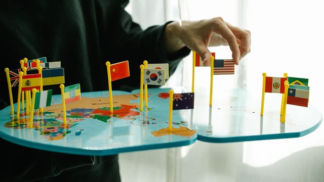 Hand arranging flags on a world map, signifying global diversity.