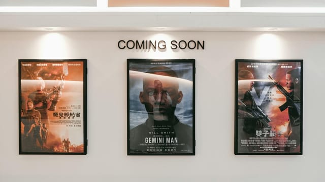 Framed posters of upcoming movies in a cinema hallway under 'Coming Soon' sign.