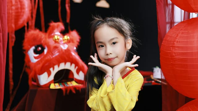 Smiling girl in traditional attire at a vibrant Lunar New Year celebration with red lanterns.