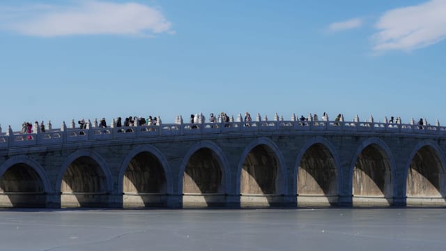 Tourists walking on the Seventeen Arch Bridge at Beijing's Summer Palace on a clear day.