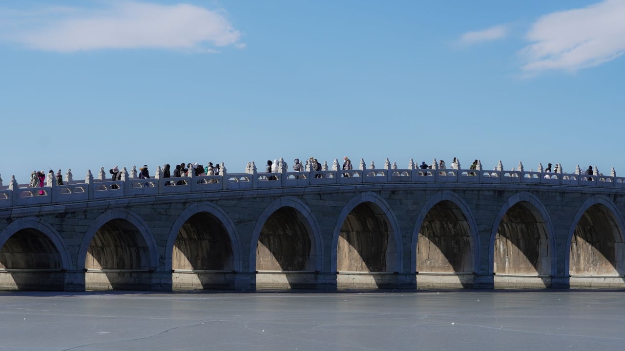 Tourists walking on the Seventeen Arch Bridge at Beijing's Summer Palace on a clear day.