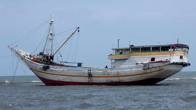 A traditional wooden cargo ship sailing in open waters under a clear sky.