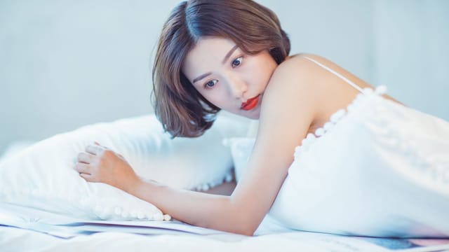 A woman resting in a serene bedroom setting, showcasing beauty and relaxation.