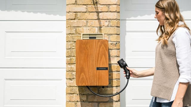 A woman uses a home electric vehicle charger mounted on a brick wall.