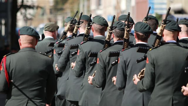 A group of soldiers in uniforms holding firearms, marching through a street in an outdoor formation.