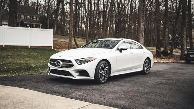 A sleek white Mercedes-Benz sedan parked on a driveway surrounded by a wooded area.