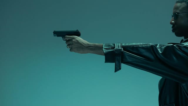 Side view of a man in a leather jacket holding a handgun, conveying a theme of defence and danger.