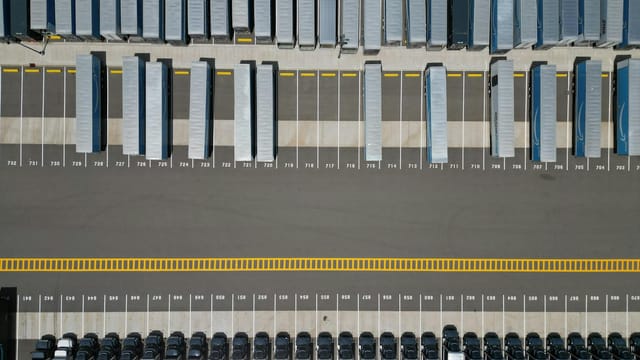High-angle shot of trucks parked in an organized grid in an industrial parking lot.