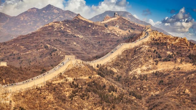 Scenic view of the Great Wall weaving through the mountainous terrain under a blue sky.