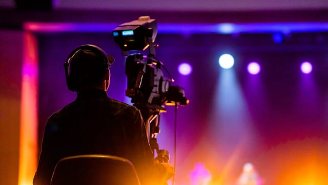 A videographer recording a live concert with vibrant spotlights, using professional equipment.