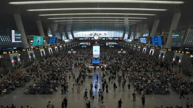 A crowded train station terminal full of travelers waiting for departures.