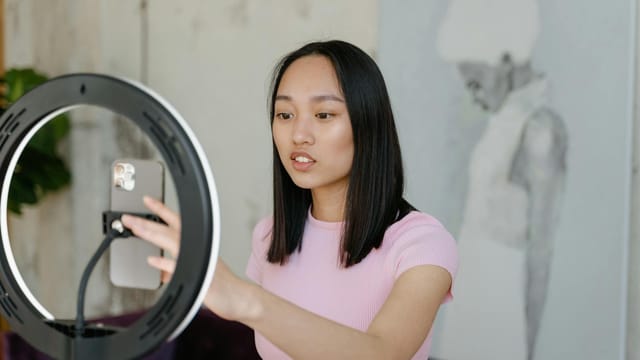 Young woman using a smartphone and ring light for social media content indoors.