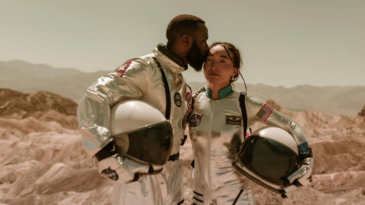 Interracial couple in space suits embracing in a desert landscape, symbolizing exploration and love.