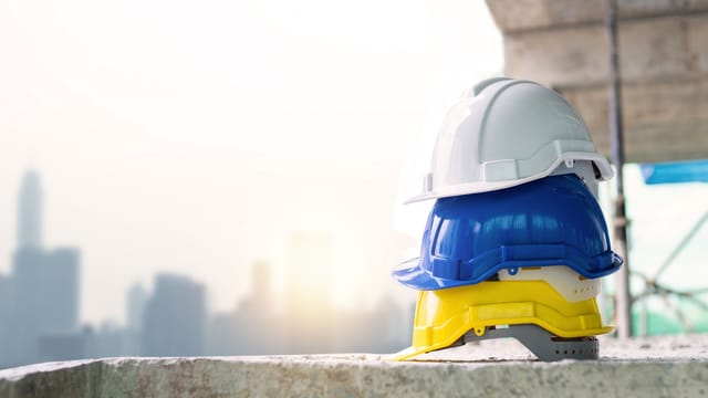 Three colorful safety helmets stacked on a concrete surface with city skyline in background.